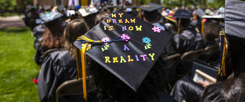 一个学生坐在他们的毕业典礼上，他们的帽读，我的梦想现在是现实。