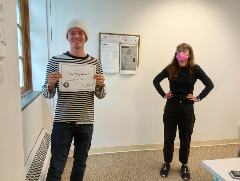 a student in a white hat holds a certificate while a woman looks on