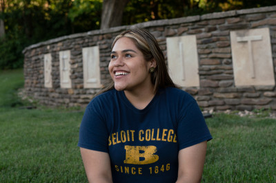 A student in Beloit gear sits in front of the Beloit College sign at the southwest side of campus...